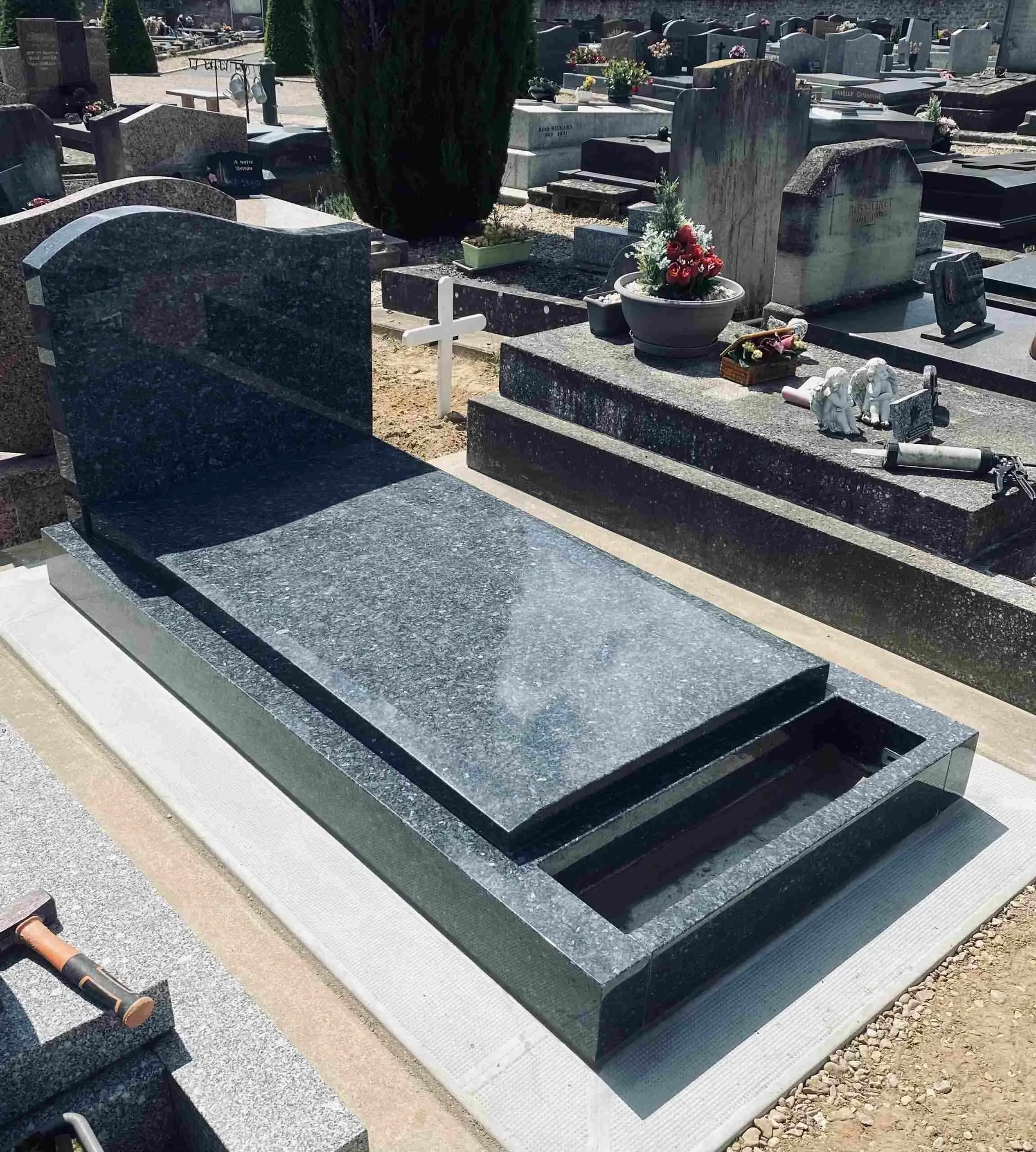 Sépulture funéraire récente en granit sombre avec jardinière intégrée.