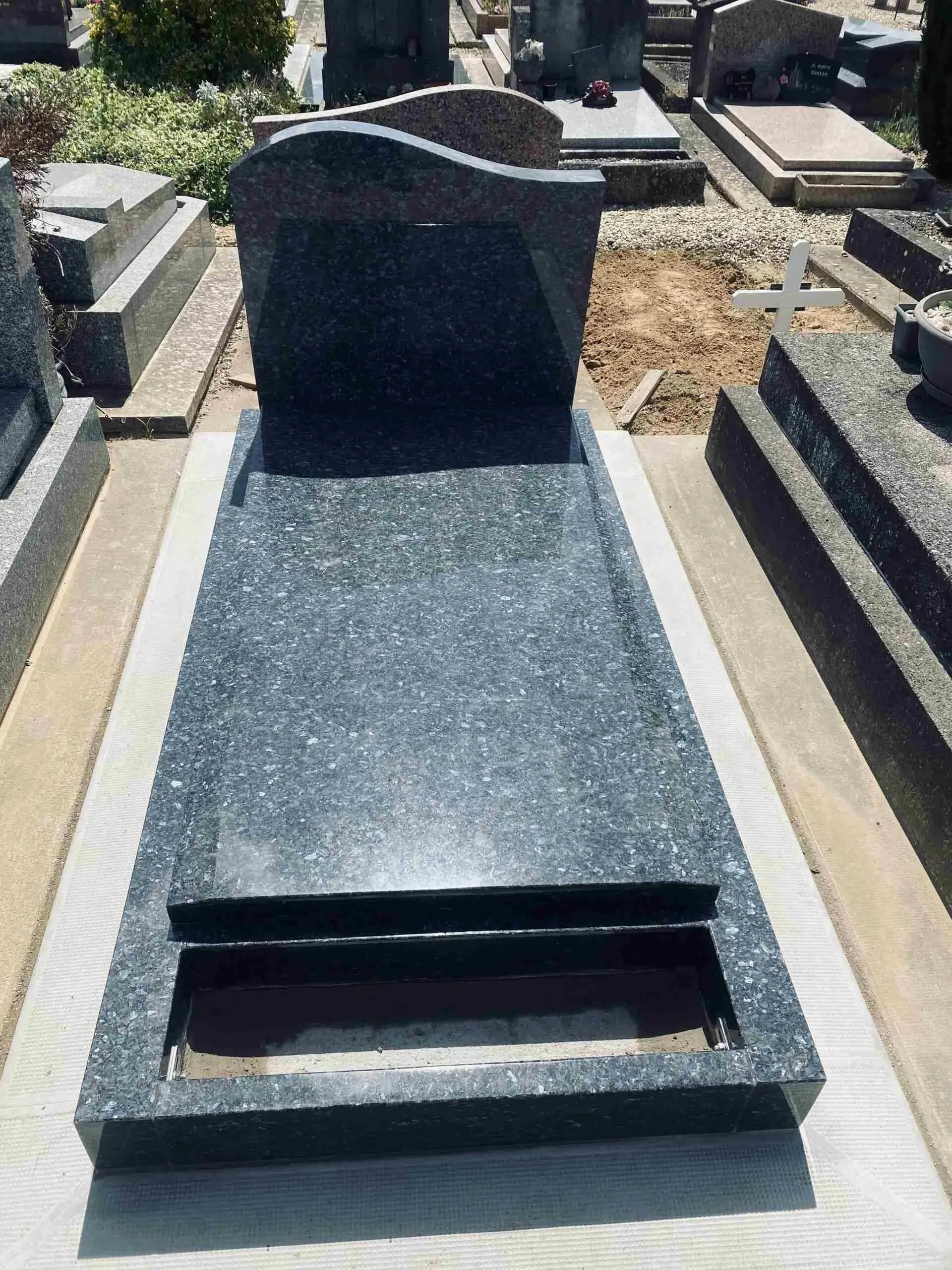Sépulture individuelle en granit bleu installée sur un emplacement en cimetière.